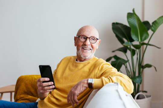 Cheerful elderly man with smartphone resting on couch