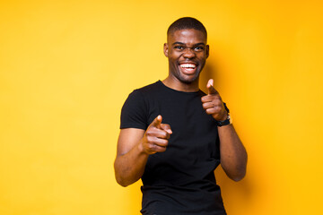 Cheerful african american man in black t-shirt smiles and points fingers at camera