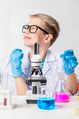Fototapeta premium A schoolboy with a microscope examines chemicals in test tubes, conducts experiments - a portrait on a white background. Concept for the study of coronavirus in the laboratory