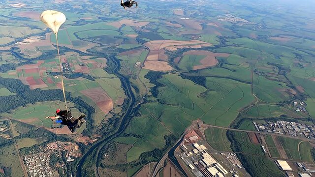 Video of a tandem parachute jump. Instructor with a student and the cameraman taking pictures. In the background there are plantations, industries and the city of Piracicaba.