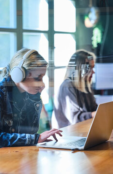 Young woman in headphones using laptop near classmate
