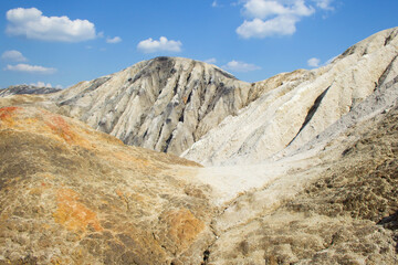 Clay, lifeless landscape against a blue sky with clouds. Open pit mining. Clay yellow, gray and black. The industrial landscape is similar to the Martian landscape.
