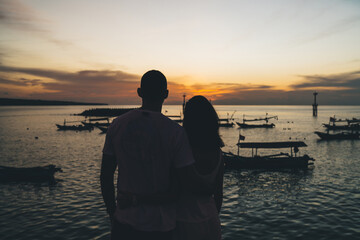 Couple embracing near rippling river with local boats in sunset