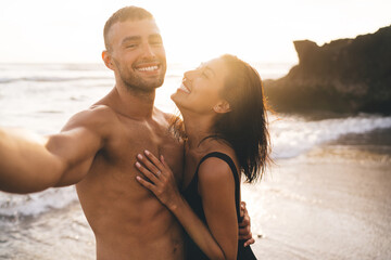 Happy diverse couple embracing on sea coast in sunlight