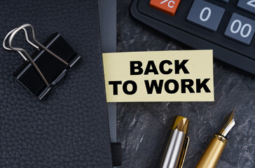 On the table is a calculator, a pen and a notebook with a bookmark on which it is written - BACK TO WORK