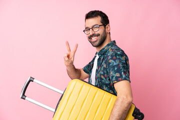 Young caucasian man over isolated background in vacation with travel suitcase and making victory...