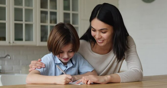 Korean mom helps to son with homework, multi ethnic family sit in kitchen schoolkid takes notes in copybook accomplish task receives from tutor praises, giving high five gesture, homeschooling concept