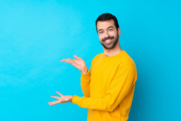 Young caucasian man over isolated blue background extending hands to the side for inviting to come