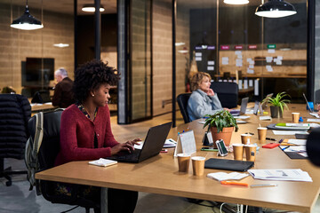 Black woman using laptop near colleagues in office