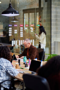 Mature employee sitting at table near colleagues