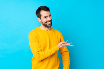 Young caucasian man over isolated blue background presenting an idea while looking smiling towards