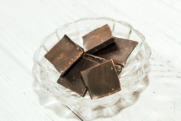 Pieces of milk chocolate in a glass plate on a light background.