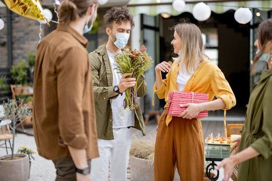 Young Adult Friends Gathering For Birthday Party At The Backyard Of Country House. Wearing Face Masks And Greet With Social Distance, New Normal During Pandemic