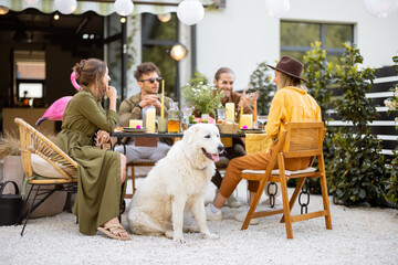A group of young friends and dog have delicious dinner, having great summertime together at the...