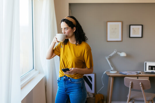Young woman drinking hot beverage near window