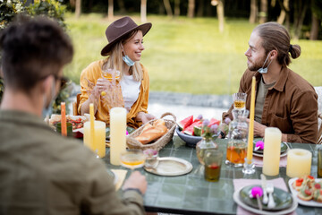 Small group of young friends in face mask have delicious dinner, having a close conversation at the backyard of the country house