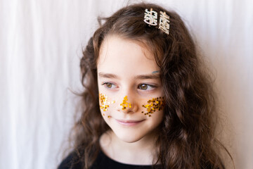 Portrait of little girl with golden glitter of stars on her face