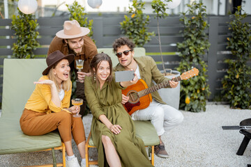 Group of young friends with drinks having fun together, making selfie or having a video call on...