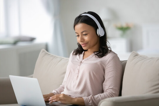 Happy African American student wearing wireless headphones, using laptop, studying from home, watching webinar, online lecture, workshop. Remote learning on internet, education, distance work concept