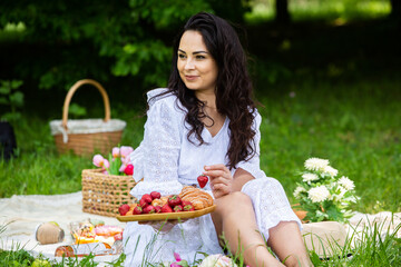 Beautiful brunette woman resting in park sitting on a picnic blanket. Relaxing in nature.