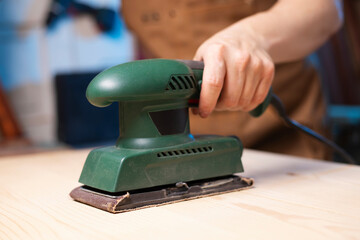 Closeup of carpenter sanding wooden planks with electrical sanding machine. A carpenter grinds wood...