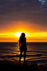 A beautiful African American woman sunrise silhouette on Lake Michigan as she looks out across the water with the orange and yellow clouds reflecting on the water below.