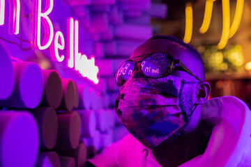Black man in mask near neon signboard