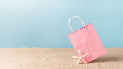 Pink color paper shopping bag on beach sand with starfish. Summer sale concept.
