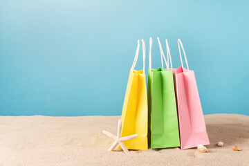 Colorful paper shopping bags on beach sand. Summer sale concept.
