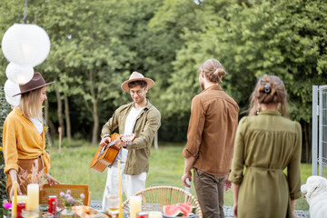 Friends hang out together on a beautiful terrace near the forest, talking and playing with dog and guitar, having great summertime