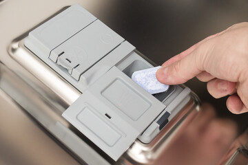 A hand puts a dishwasher tablet into the detergent tray.