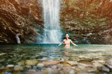 Young beauty in a swimsuit bathes near a waterfall.