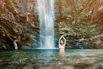 Beautiful joyful woman in a swimsuit posing at the camera near the waterfall.