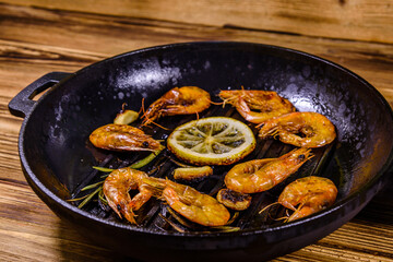 Roasted shrimps with lemon slice, garlic and rosemary in a cast iron pan