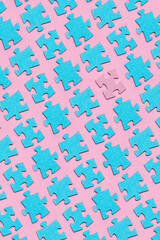 A lot of identical disconnected turquoise puzzles with one pink one located diagonally on a pink background.