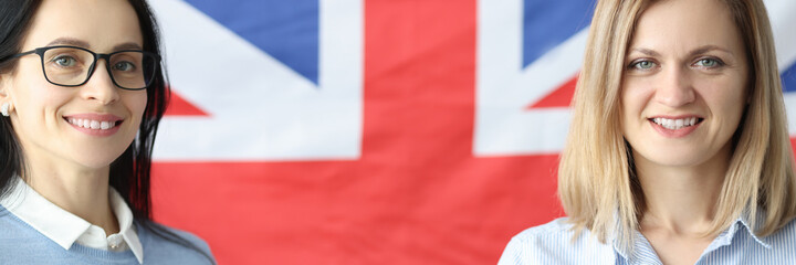 Two smiling women stand with notebooks in front of British flag