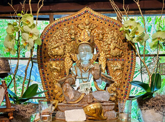 Obraz premium Gold Glass Buddha sculpture with money with candle decorations and orchids indoors with garden behind