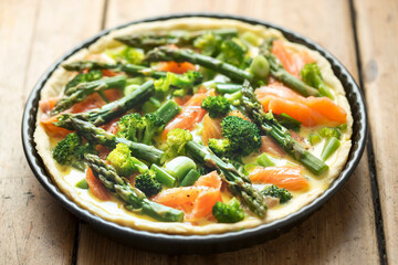 Preparing quiche with salmon, broccoli and green asparagus, coated with milk and eggs mixture. Raw tart - oven ready. 