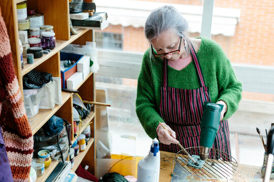 Senior woman applying patina to a bronze piece with a brush and hot air