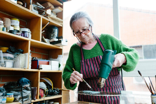 Senior Woman Applying Patina To A Bronze Piece With A Brush And Hot Air