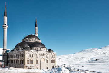 Fototapeta na wymiar Mosque against snowy valley and blue sky.