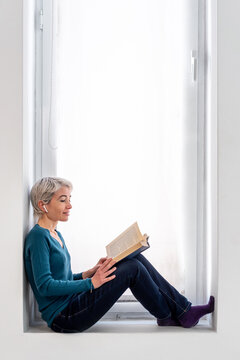 Woman reading book against window