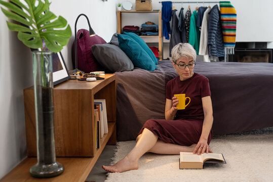 Woman with mug reading book near bed