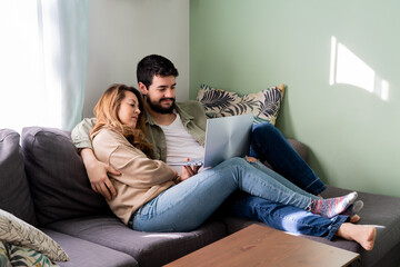 Happy couple at home watching movie on laptop in living room enjoying free time