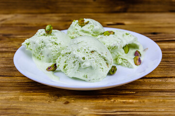 Glass bowl with pistachio ice cream balls and nuts on a wooden table