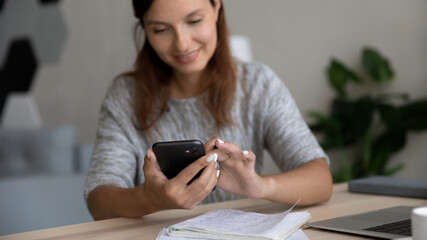 Close up smiling woman using smartphone, sitting at workplace with notebooks, confident businesswoman looking at phone screen, browsing apps, chatting in social networks, distracted from work