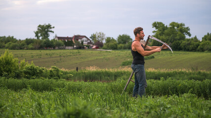 Side view of farmer holding grindstone and scythe on grassy field 