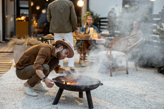 Man Grilling Meat On A Bbq, Having A Festive Evening Snack With Friends At Backyard Of A Country House