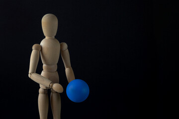 A wooden dummy holds a blue ball. Black background, close-up, copy space, horizontal orientation.