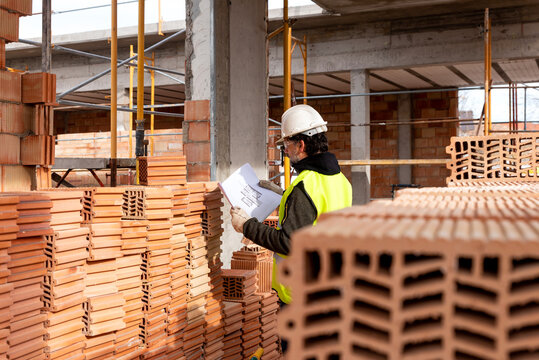 Construction worker with blueprint standing near stack of bricks